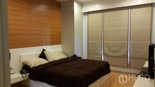 Condominium for rent in Khlong Toei, Bangkok - Spacious master bedroom with wood accent wall, blackout blinds and king-sized bed.