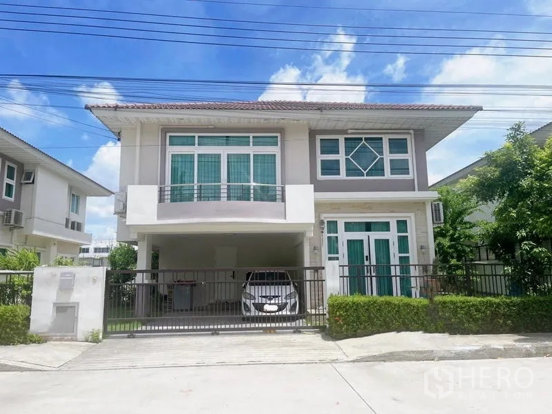 บ้าน ขายในBang Phli, Samut Prakan - บ้านเดี่ยวสองชั้นสไตล์โมเดิร์น ด้านหน้ามีระเบียง ทางเข้ามีรั้ว และโรงจอดรถมีหลังคา ในวันที่ท้องฟ้าแจ่มใส