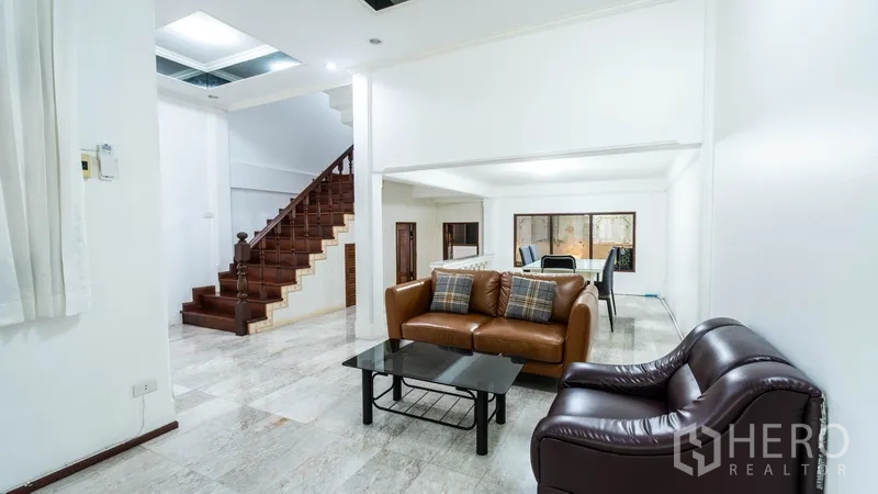 Townhouse for rent in Watthana, Bangkok - Spacious living area with leather sofas and a wooden staircase.