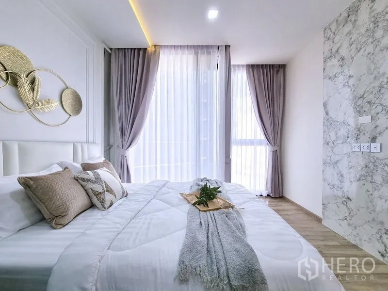 คอนโด ขาย - มุมห้องนอน หน้าต่างใหญ่ ม่านสีเทา และผนังลายหินอ่อน