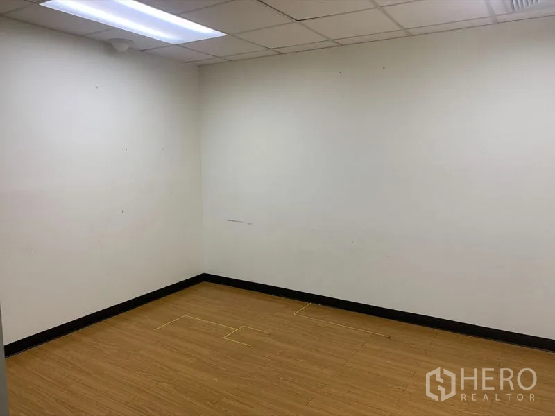 Office Space for rent in Bang Rak, Bangkok - Compact private office with wood-style flooring and clean white walls under fluorescent lighting.