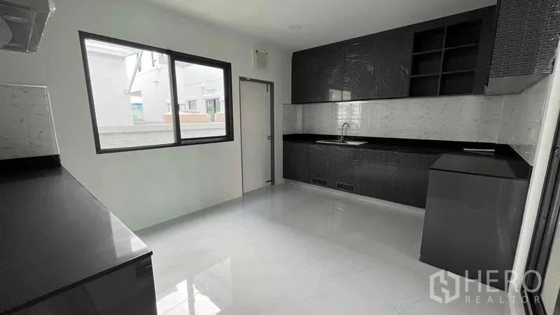Detached House for sale in Bang Phli, Samut Prakan - Modern closed kitchen with black cabinetry, stone countertop and a bright window.