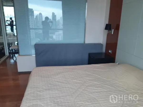 Condominium for rent or sale in Khlong Toei, Bangkok - Master bedroom reverse view showing glass partition with blinds and bedside table.
