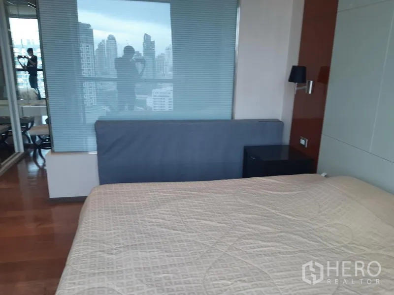 Condominium for rent or sale in Khlong Toei, Bangkok - Master bedroom reverse view showing glass partition with blinds and bedside table.