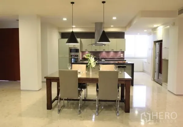Condominium for rent in Khlong Toei, Bangkok - Open-plan kitchen with island, pendant lights and a wooden dining table in a modern Bangkok condo.