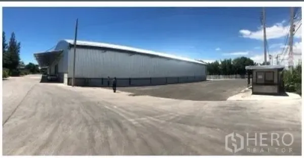 Warehouse for rent in Chon Buri - Metal-clad warehouse exterior in Si Racha with a wide truck yard and guard booth under a clear sky.