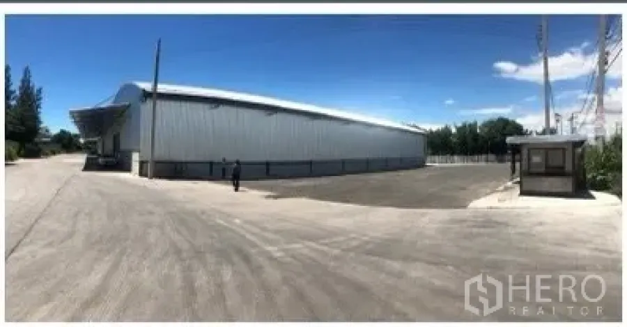 Warehouse for rent in Chon Buri - Metal-clad warehouse exterior in Si Racha with a wide truck yard and guard booth under a clear sky.