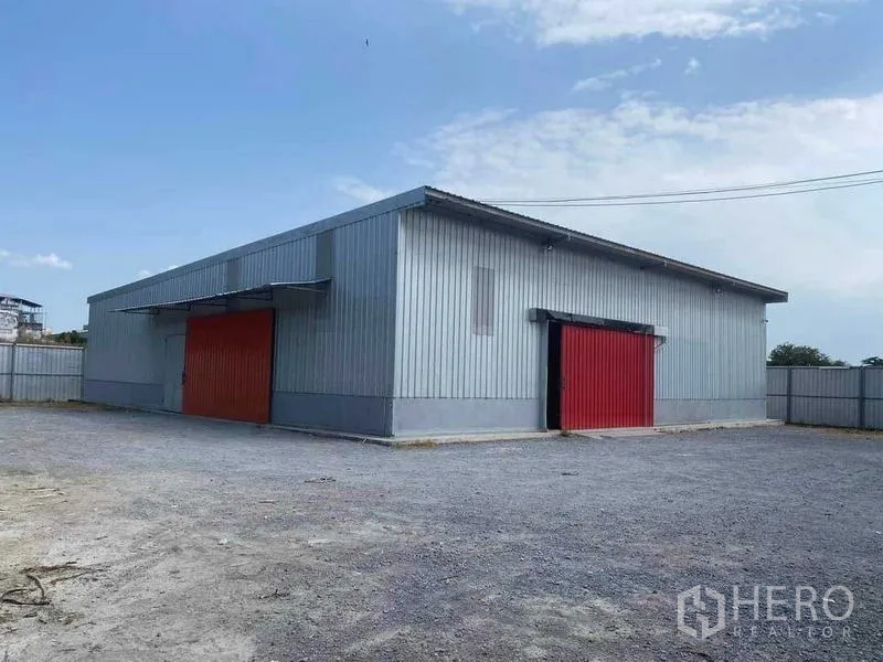 Warehouse for rent in Nong Khaem, Bangkok - Metal-clad warehouse with two red sliding doors and a large gravel yard in Nong Khaem, Bangkok.