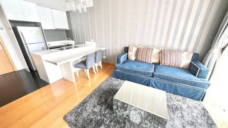 Condominium for rent or sale in Watthana, Bangkok - Open-plan living and dining area with blue sofa, breakfast bar and wood floors.