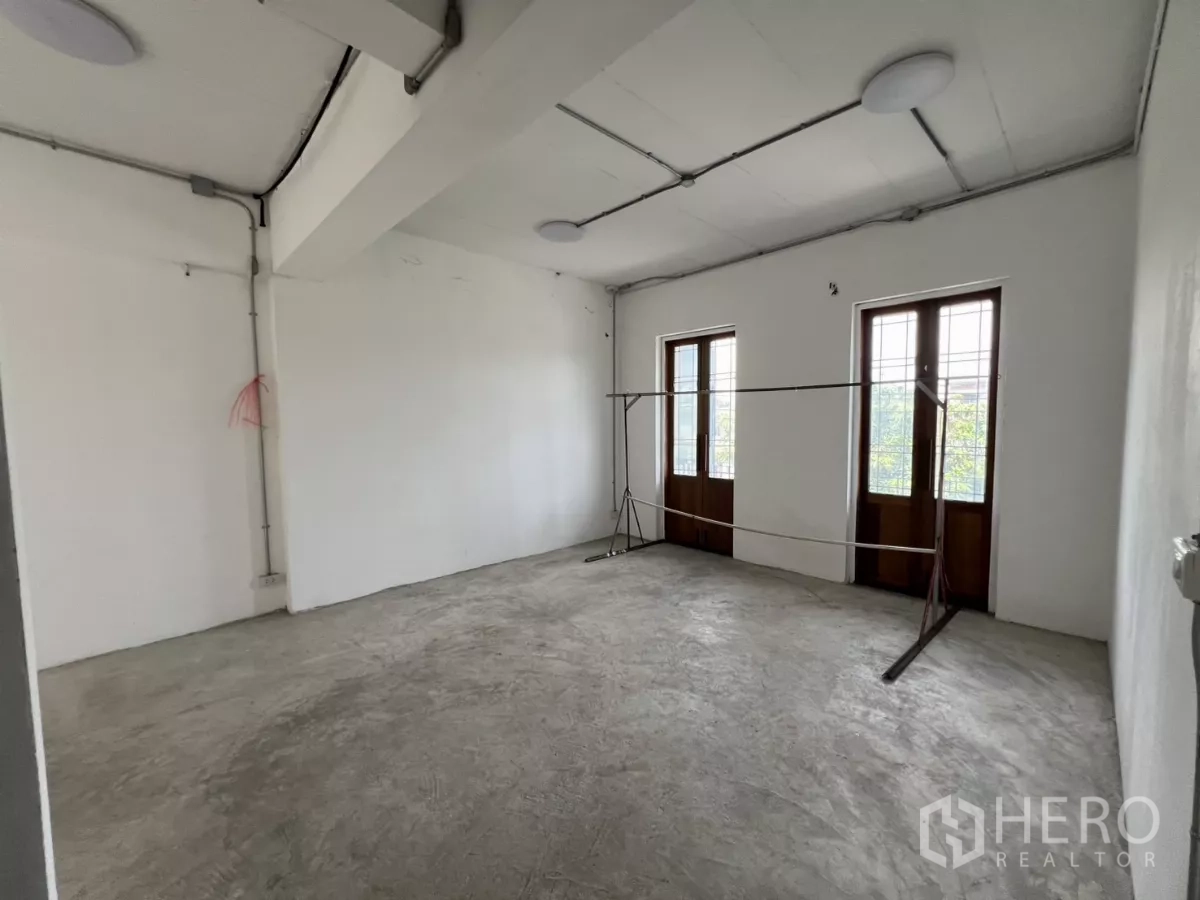 Retail Space for rent in Khlong Toei, Bangkok - Spacious white room with two wooden French windows and an exposed-conduit ceiling.