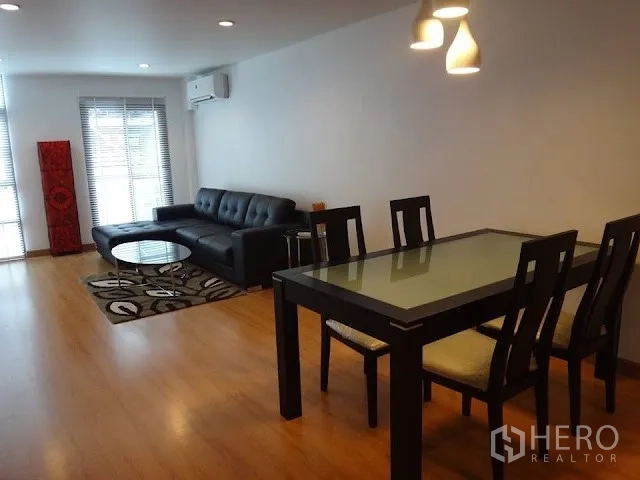 Condominium for rent in Bang Rak, Bangkok - Spacious living and dining area with pendant lights, a glass-top table, and a sectional sofa on warm wood flooring.