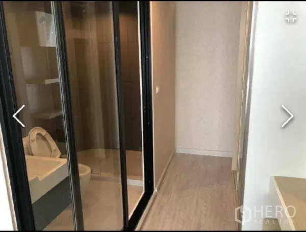 Condominium for rent in Watthana, Bangkok - Modern bathroom with glass sliding doors and shower enclosure beside a light wood hallway.