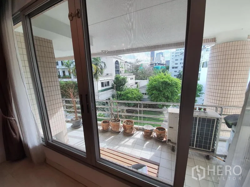 Condominium for rent in Pathum Wan, Bangkok - Covered balcony with railing, potted plants, and green neighborhood views.