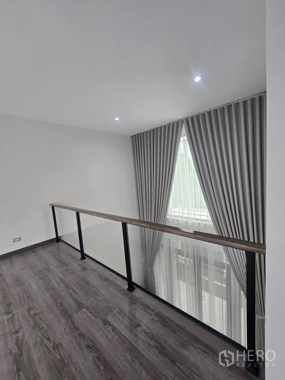 บ้านแฝด for rent in Suan Luang, Bangkok - พื้นที่ชั้นลอยพร้อมราวกระจก มองลงสู่โถงเพดานสูงและผ้าม่านทิ้งตัว.
