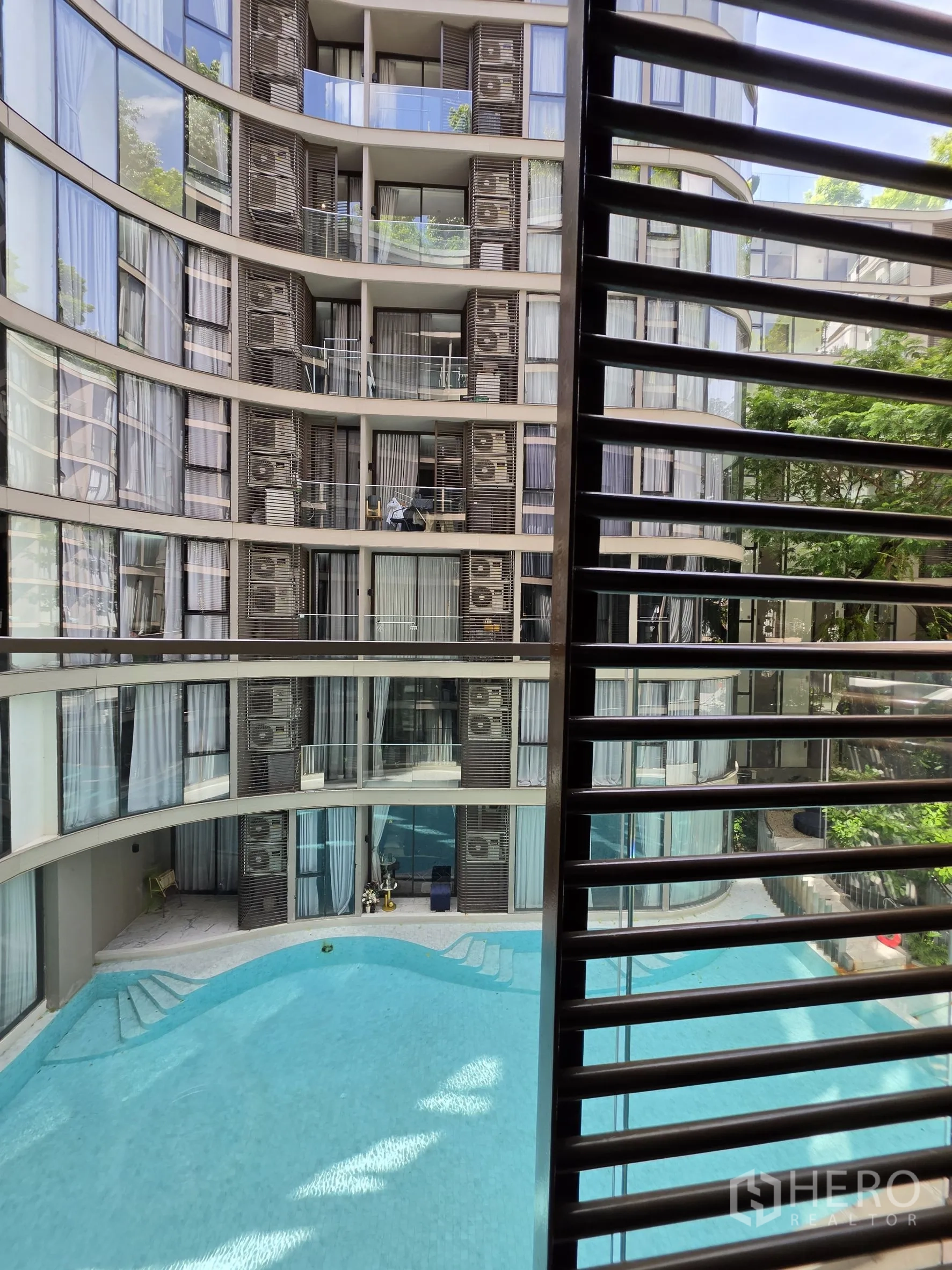 Condominium for rent in Khlong Toei, Bangkok - Balcony view through a louvered screen overlooking a swimming pool.