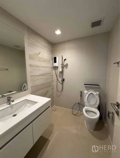 Townhouse for rent in Lat Phrao, Bangkok - Neutral-tone bathroom with vanity, toilet and walk-in shower with water heater.