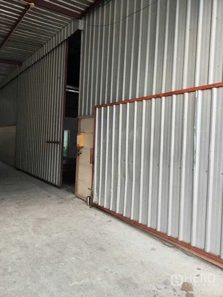 货栈 出租在Bang Kapi, Bangkok - 邦甲比仓库入口，带大型金属推拉门与波纹金属外墙。