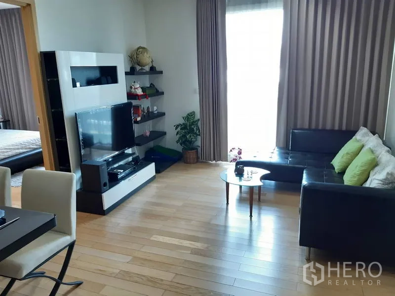 Condominium for rent in Khlong Toei, Bangkok - Bright living room featuring an L-shaped leather sofa, TV console, floating shelves and full-length curtains.