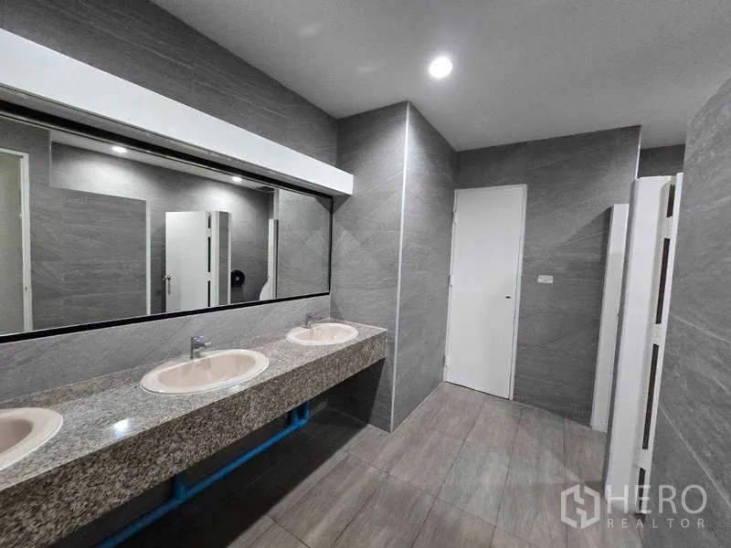 Office Space for rent in Khlong Toei, Bangkok - Modern shared restroom with long granite vanity, mirrors and grey tiles.