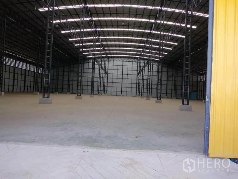 Factory for rent in Mueang Samut Prakan, Samut Prakan - Wide entry to the factory showing a yellow sliding door and illuminated high roof structure.