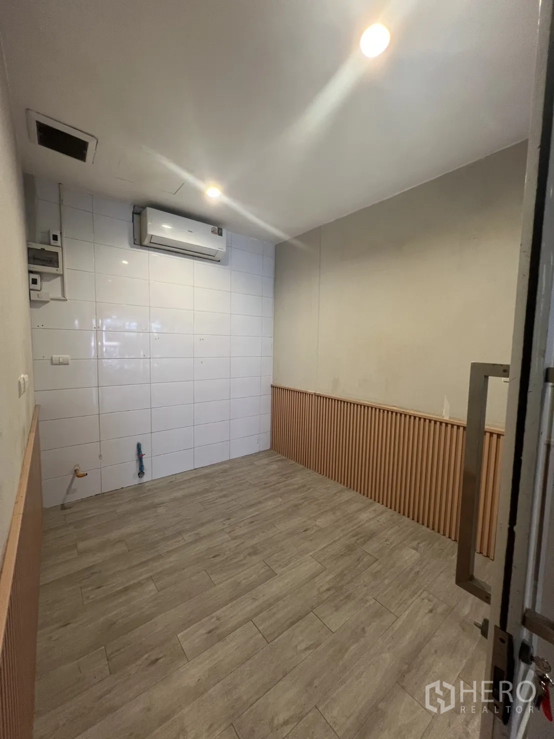 Retail Space for rent in Watthana, Bangkok - Narrow shop interior with AC, tiled accent wall with wainscoting, wood-look floor, and utility connections near the entrance.