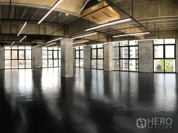 Office Space for rent in Khlong Toei, Bangkok - Open-plan loft office with polished black epoxy floors, exposed concrete ceiling, linear LED lighting, and floor-to-ceiling windows with city views.