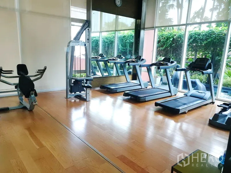 Condominium for rent or sale in Watthana, Bangkok - Fitness room with treadmills and exercise machines overlooking a garden.