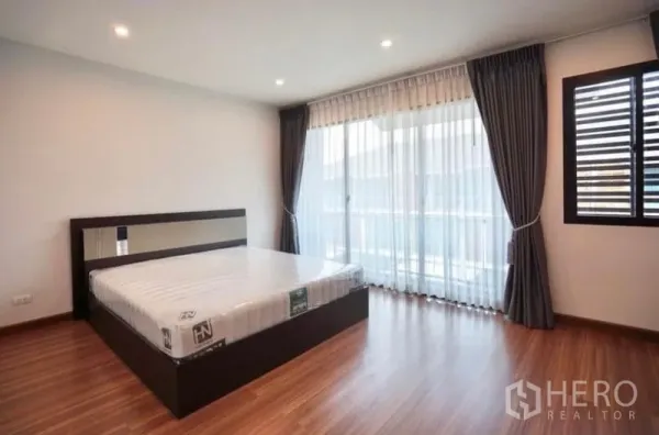 Townhouse for rent in Bang Kapi, Bangkok - Bright bedroom with king bed, wood floors and floor-to-ceiling sheer curtains opening to a balcony.