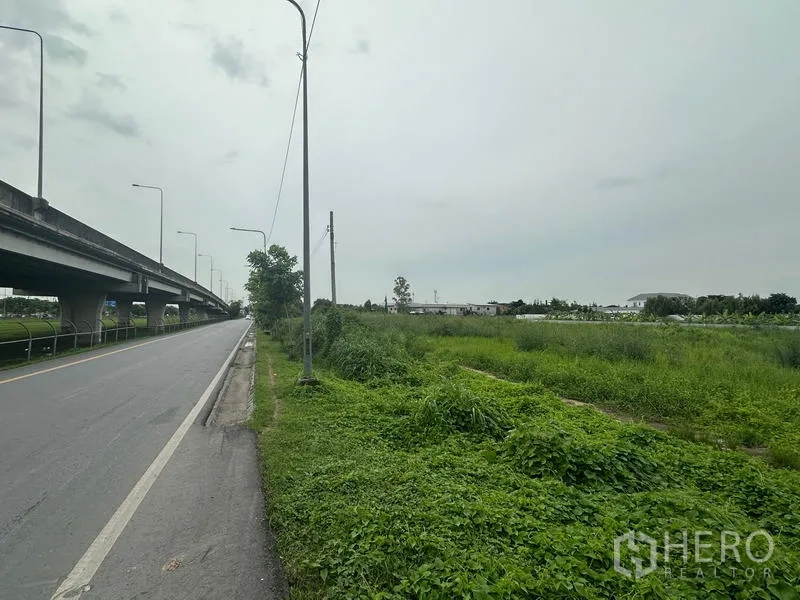 ที่ดิน ขายในSai Mai, Bangkok - ด้านหน้าแปลงติดถนนข้างทางยกระดับ มีเสาไฟฟ้าและพื้นที่ว่างฝั่งขวา เขตสายไหม