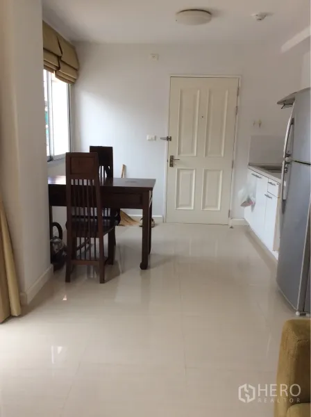 公寓 出售在Pathum Wan, Bangkok - 开放式小厨房，白色橱柜与木质餐桌，面向入户门。