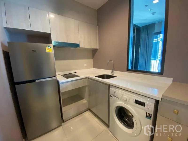 Condominium for rent in Pathum Wan, Bangkok - Compact L-shaped kitchen with sink, cooktop, fridge and washing machine.