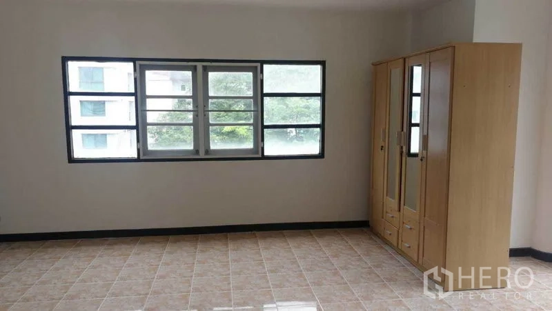 Townhouse for rent in Khlong Toei, Bangkok - Sunlit room with wide window and freestanding wardrobe on tiled floor.