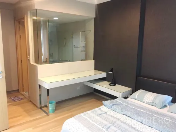 Condominium for rent in Khlong Toei, Bangkok - Bedroom featuring built-in vanity, glass-partitioned bathroom, and light wood flooring.
