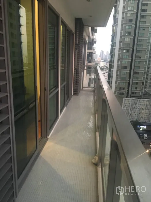 Condominium for rent in Khlong Toei, Bangkok - Long balcony with glass railing overlooking neighboring towers and the Bangkok skyline.