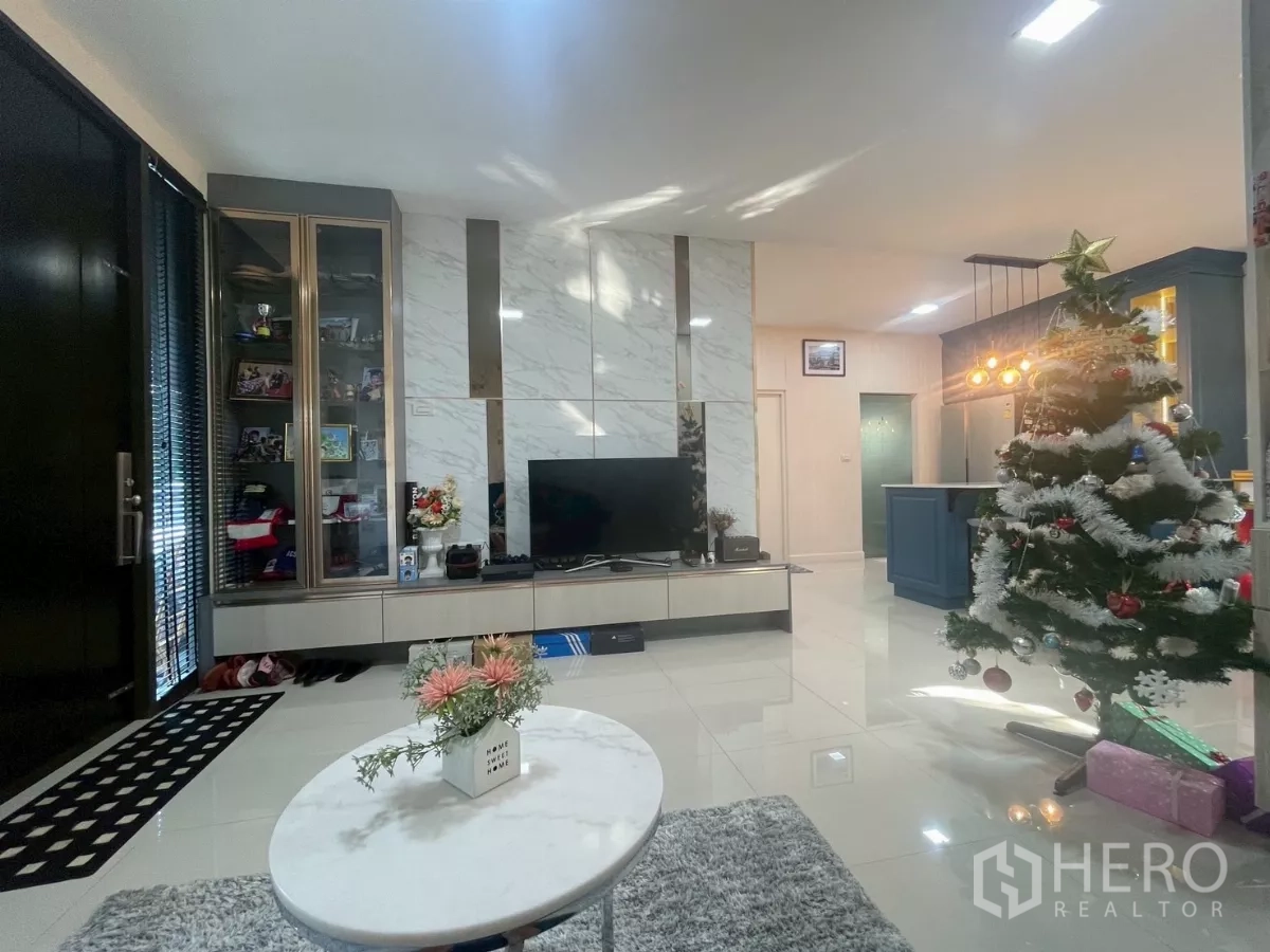 บ้าน ขายในBang Phli, Samut Prakan - ห้องรับแขกสว่าง ผนังทีวีลายหินอ่อน ตู้กระจก และวิวต่อเนื่องสู่ครัวไอส์แลนด์ มีต้นคริสต์มาส