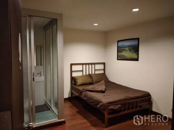 Shophouse for rent in Watthana, Bangkok - Compact bedroom with wooden bed, brown linens, and en-suite behind glass sliding doors.