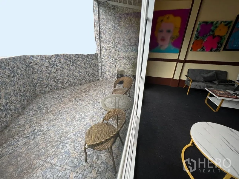 Shophouse for rent in Khlong Toei, Bangkok - Tiled balcony terrace with rattan chairs beside sliding glass doors.