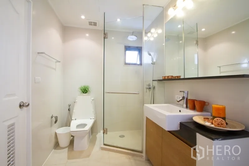 Apartment for rent in Watthana, Bangkok - Contemporary bathroom with glass-enclosed rain shower, wide mirror, vanity and toilet.