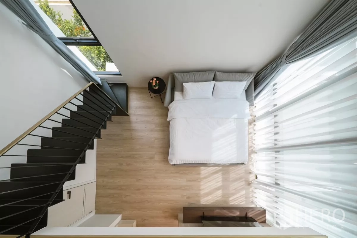 Detached House for rent or sale in Saphan Sung, Bangkok - Top-down view of double-height bedroom with bed by tall curtains and stairs.