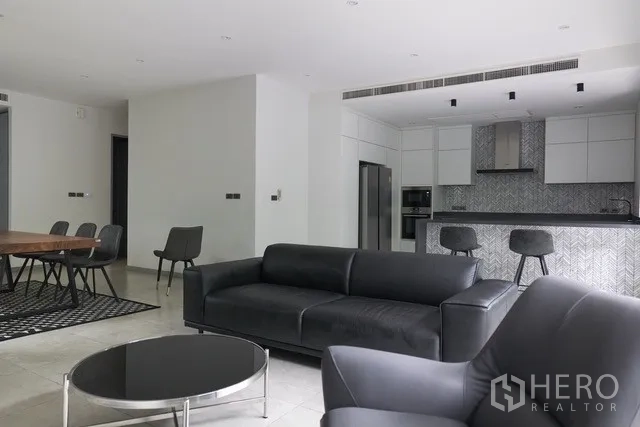 Townhouse for sale in Watthana, Bangkok - Open-plan living and kitchen with black leather sofas, dining area and tiled floors.