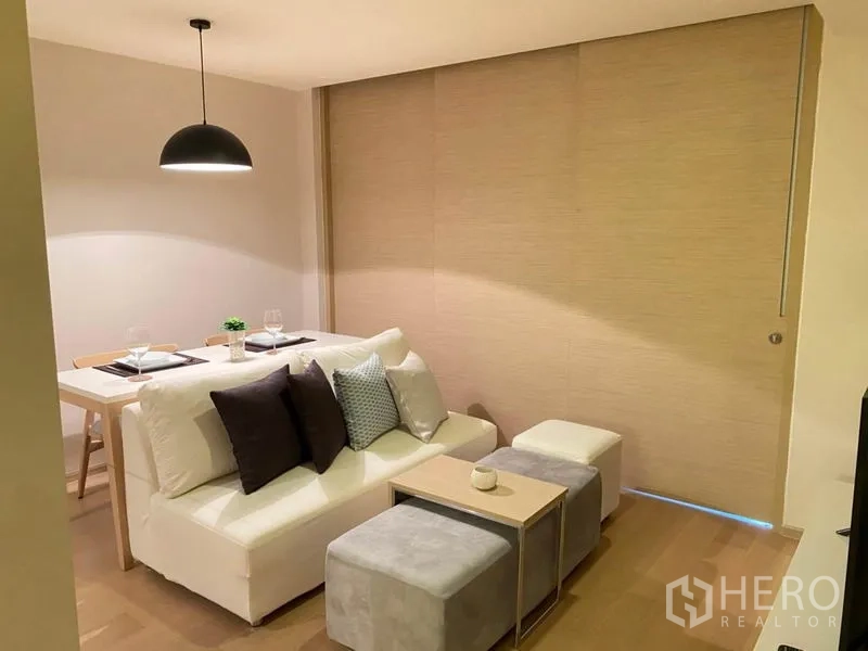 公寓 出租在Watthana, Bangkok - 紧凑客厅区，沙发、脚凳和吊灯下的用餐角。