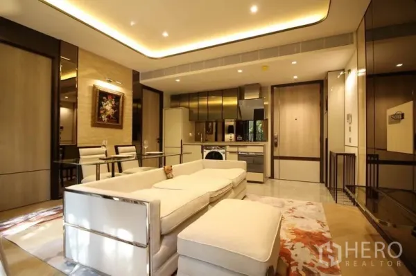 公寓 出租在Watthana, Bangkok - 开放式起居区，沙发与脚凳面向现代厨房，内置家电与氛围灯光。