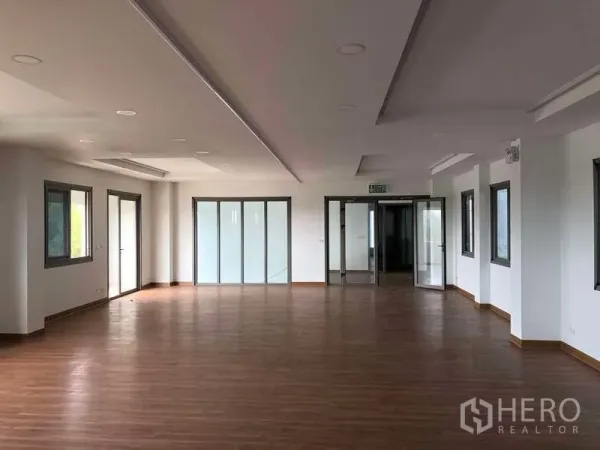 Factory for rent or sale in Samut Prakan - Bright open-plan office with wood flooring, windows and glass doors.