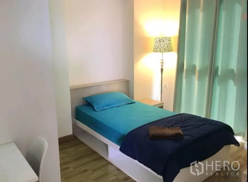 Condominium for rent in Phra Khanong, Bangkok - Second bedroom with single bed, teal bedding, study desk, floor lamp and full-height drapes by the window.