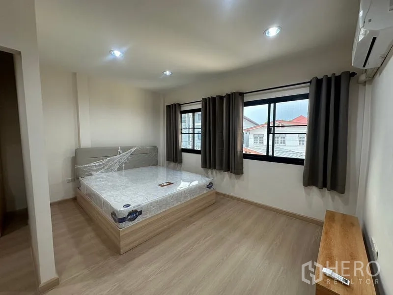 Townhouse for rent or sale in Phra Khanong, Bangkok - Bright bedroom with bed by two windows and blackout curtains.