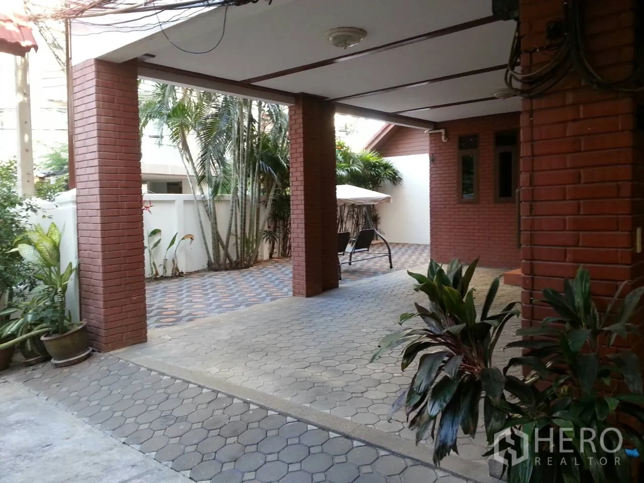 Townhouse for rent or sale in Watthana, Bangkok - Covered carport and driveway with garden seating beside a red-brick townhouse.