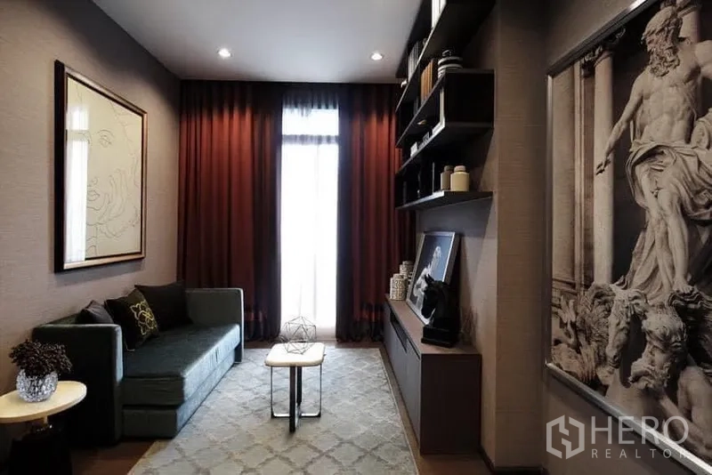 Condominium for rent in Bang Rak, Bangkok - Elegant living area with sofa, built-in shelving, framed art, and soft lighting facing a tall window.