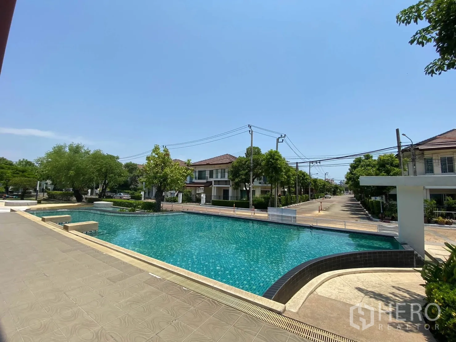 独栋房屋 for rent in Mueang Samut Prakan, Samut Prakan - 社区大型室外泳池，周边为低层住宅与绿树。