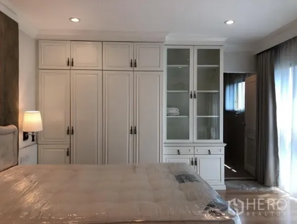 Condominium for rent or sale in Sathon, Bangkok - Bedroom with full-height built-in wardrobes and glass display cabinet leading to an en-suite.