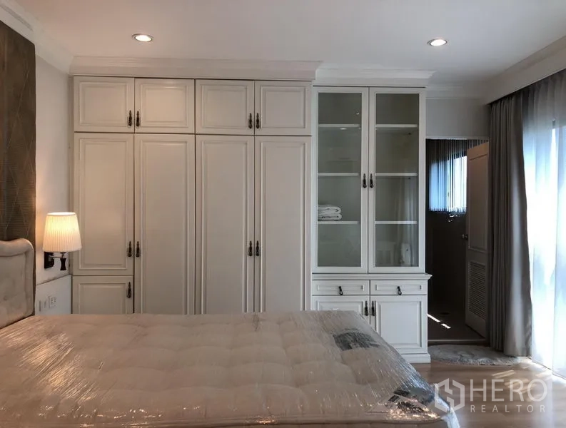 Condominium for rent or sale in Sathon, Bangkok - Bedroom with full-height built-in wardrobes and glass display cabinet leading to an en-suite.